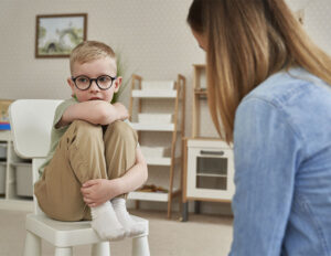 little boy with autism sitting in a chair and looking away